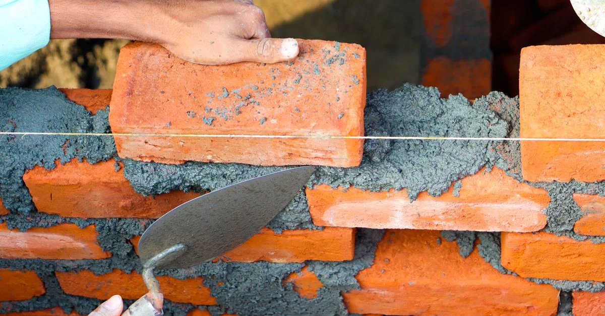 Mains posant des briques avec du ciment dans un environnement de construction, mettant en valeur un travail de maçonnerie précis.