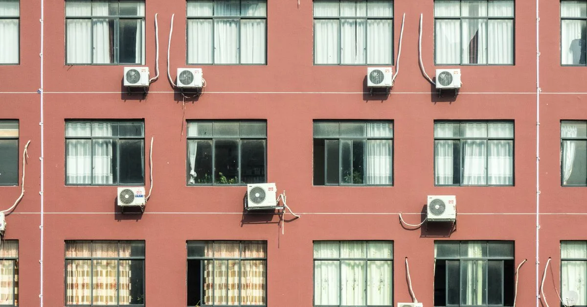 Façade d'immeuble rouge avec plusieurs fenêtres et climatiseurs, mettant en valeur l'architecture urbaine.