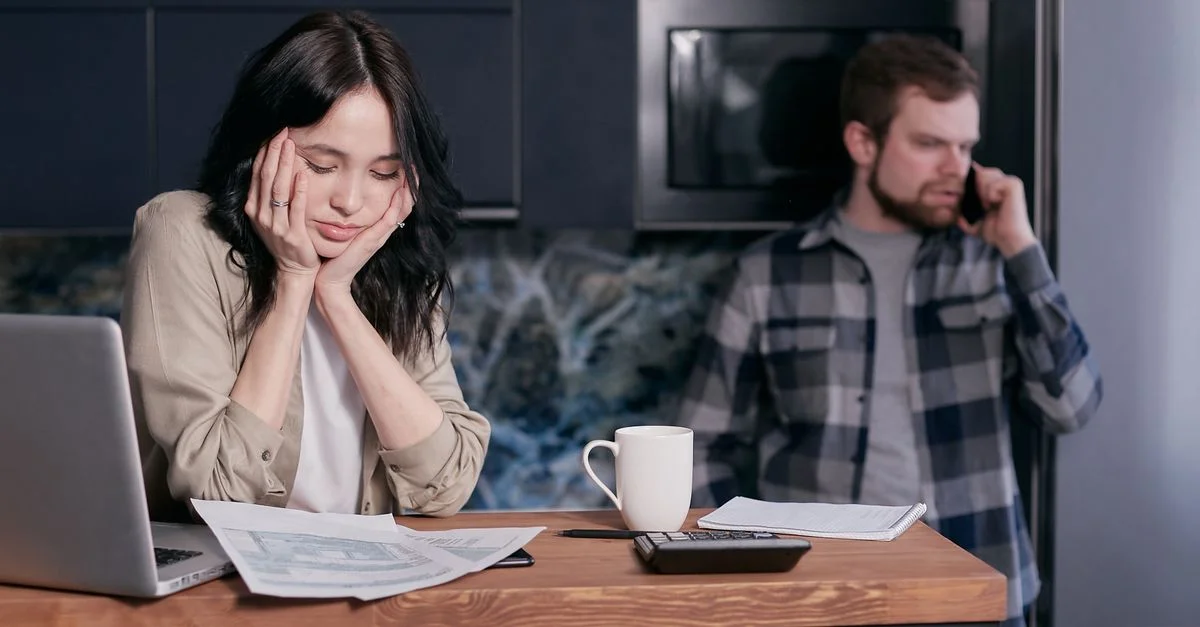 Un couple confronté à un stress financier, entouré de factures et d'un ordinateur portable à l'intérieur.