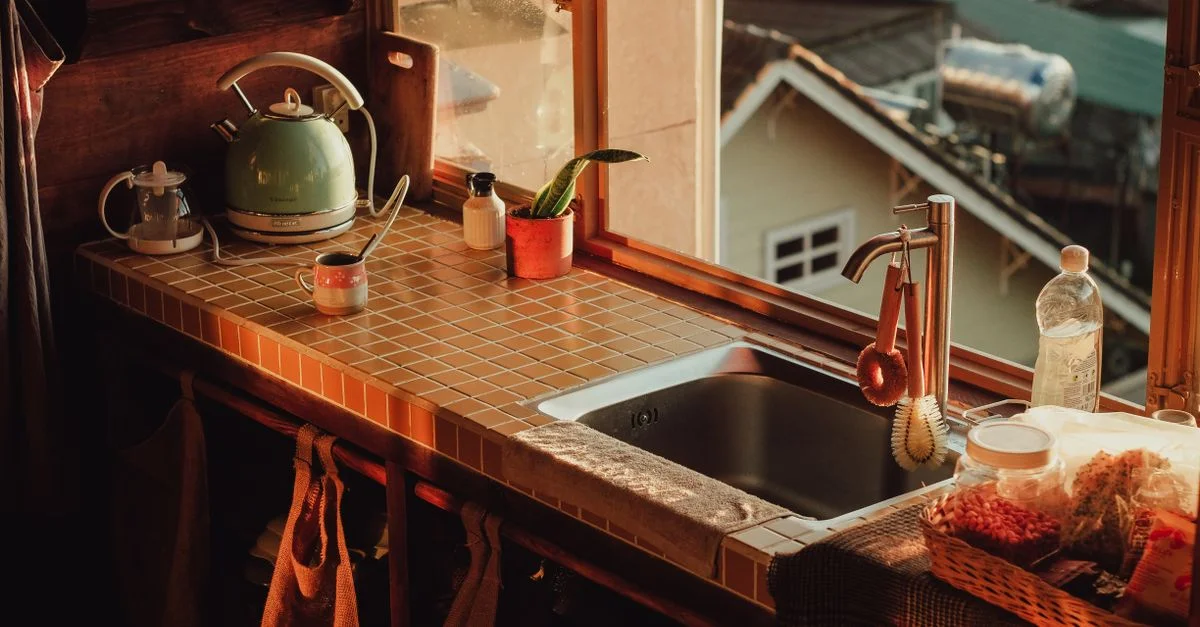 Plan de travail de cuisine chaleureux avec une bouilloire, un évier et de la lumière naturelle. Parfait pour la photographie conviviale.