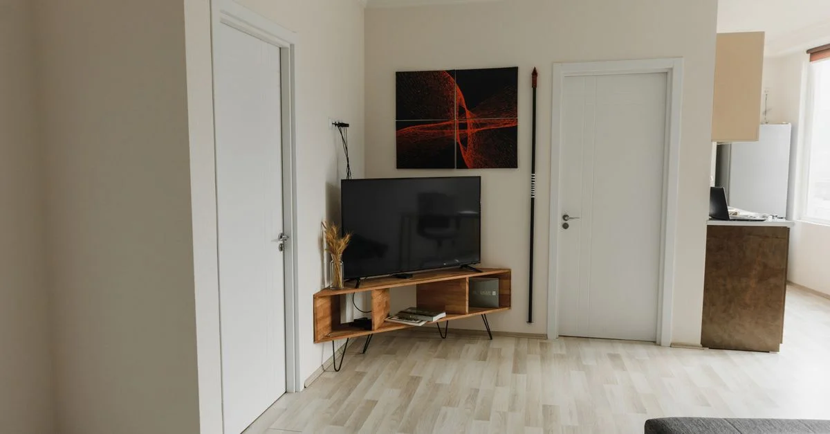 Un salon moderne et minimaliste avec TV, œuvres murales et un sol en bois, offrant un aspect propre et organisé.