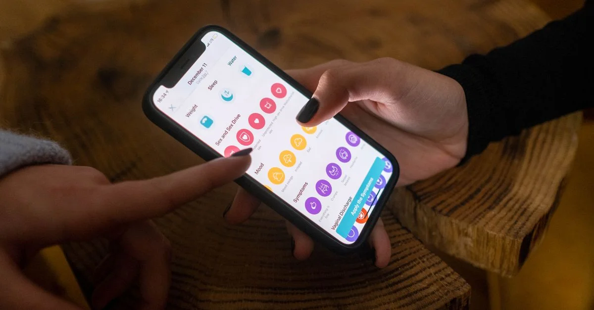 Gros plan sur des mains utilisant une application de suivi de fertilité sur un smartphone à l'intérieur.