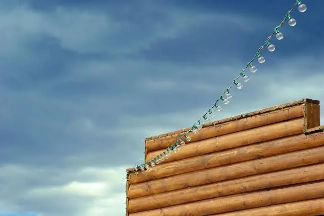 Un mur de cabine en bois décoré de guirlandes lumineuses sur fond de ciel nuageux dramatique.