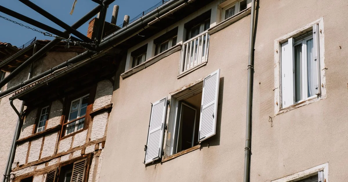 La façade d'un bâtiment européen vintage avec des volets ouverts et des poutres en bois sous un ciel dégagé.