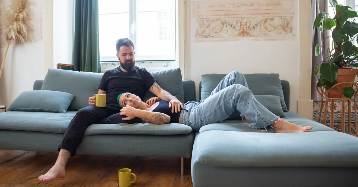 Couple se relaxant sur un canapé avec des tasses de café, ayant l'air cosy et à l'aise, incarnant la détente et la romance à l'intérieur.
