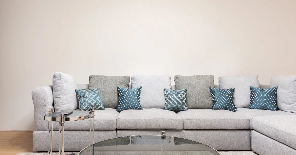 Un salon contemporain avec un canapé sectionnel gris, des coussins à motifs et une table basse en verre ronde.
