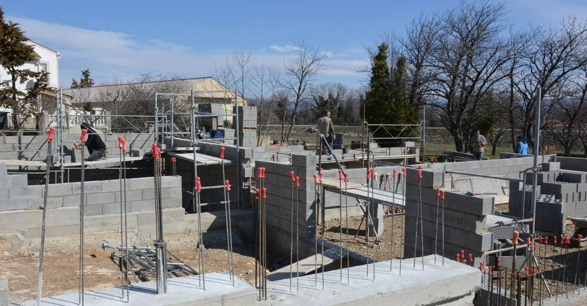Chantier ensoleillé avec des travailleurs sur une fondation en béton sous un ciel bleu clair.