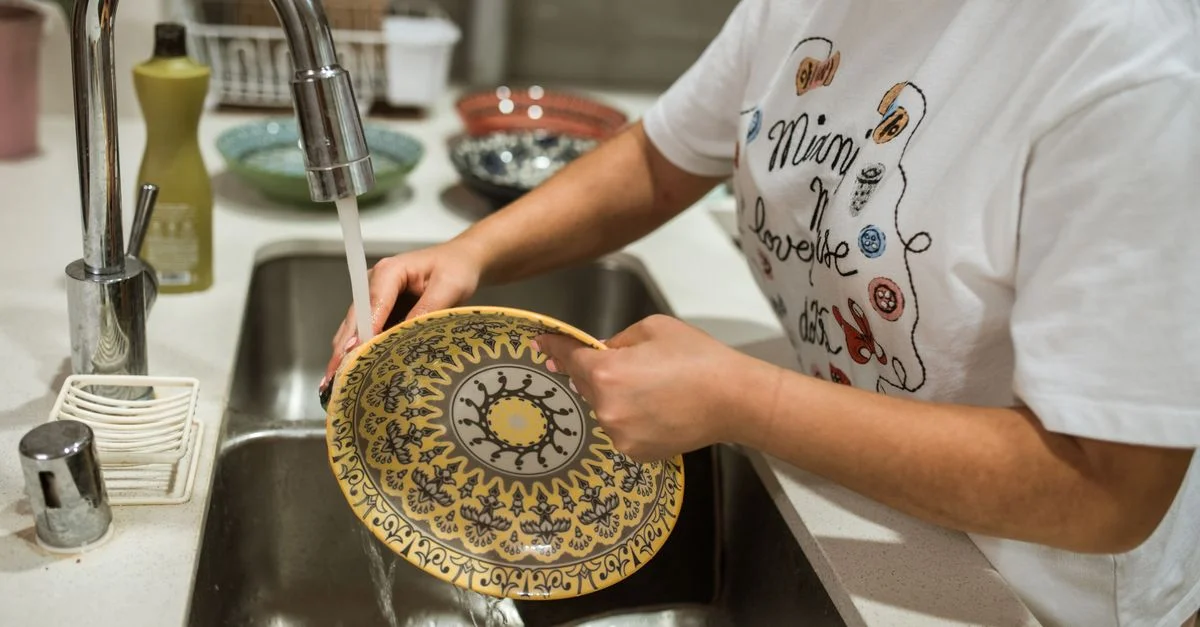 Gros plan sur des mains lavant une assiette décorative dans un évier de cuisine moderne.