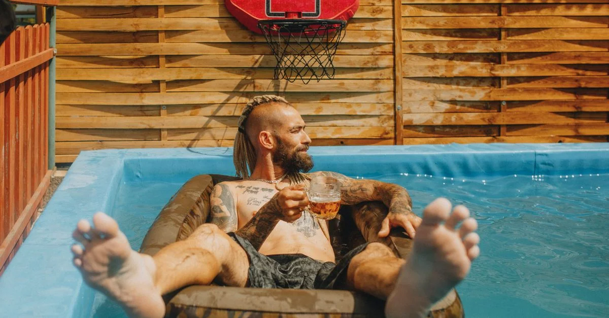 Homme se détendant sur un gonflable dans une piscine extérieure avec un verre, ambiance estivale.