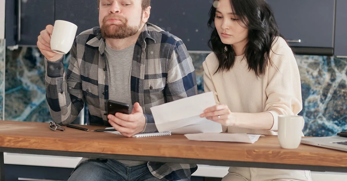 Un couple examine des factures ensemble dans une cuisine moderne tout en dégustant du café, créant une atmosphère chaleureuse et intime.