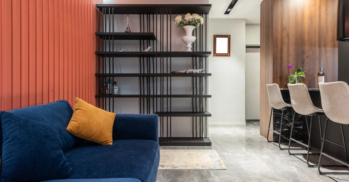 Salon contemporain avec canapé bleu, mur orange strié et élégante étagère noire.