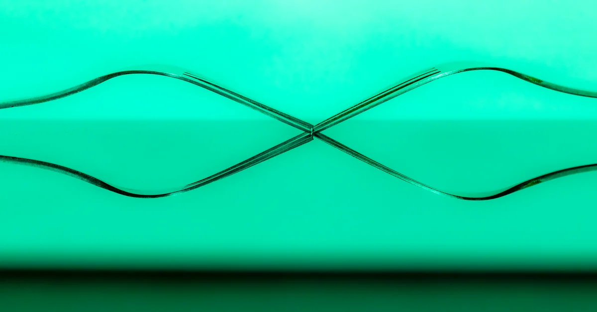 Deux fourchettes formant un motif abstrait symétrique sur un fond vert.
