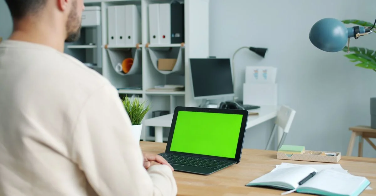 Aménagement d'un bureau à domicile avec un homme utilisant un ordinateur portable à fond vert.
