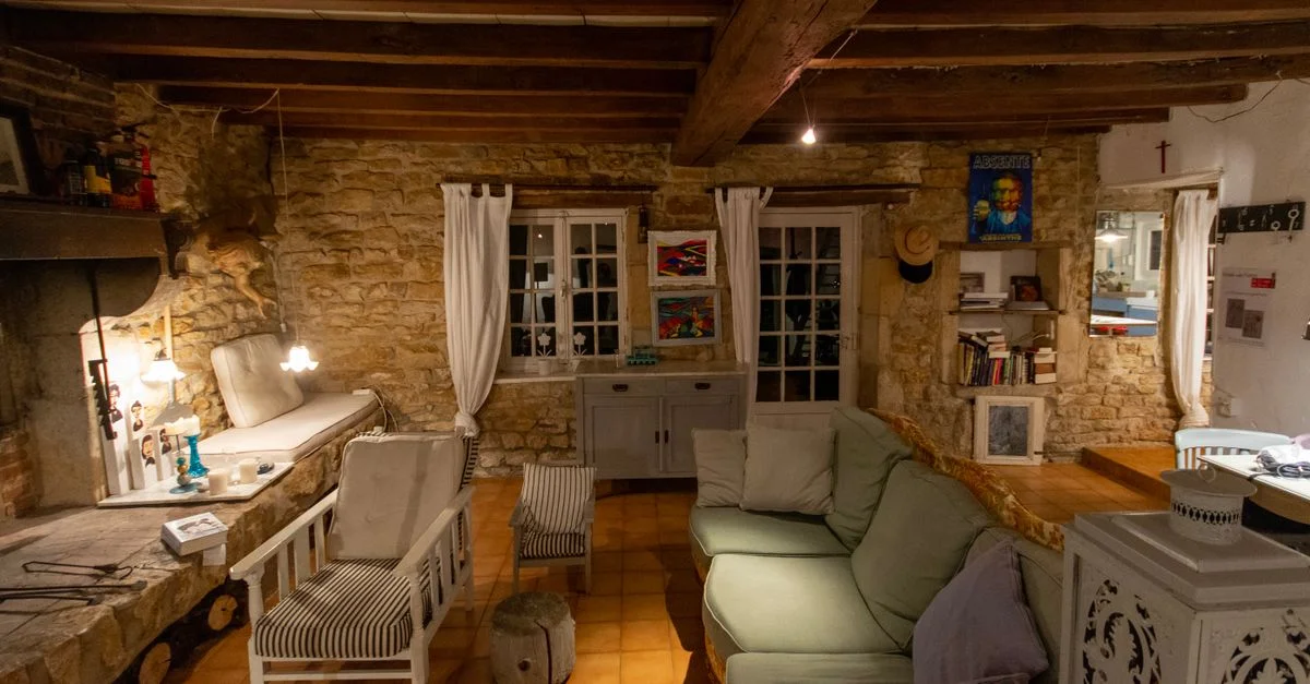 Salon rustique chaleureux avec murs en pierre, poutres en bois, fauteuils et canapé créant une ambiance confortable.