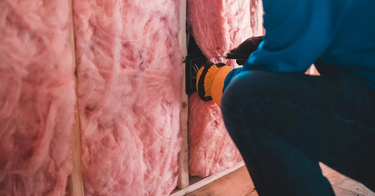 Travailleur concentré installant une isolation en fibre de verre rose à l'intérieur d'un bâtiment.